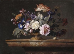 Flowers in a glass vase with metal mounted foot on a marble ledge